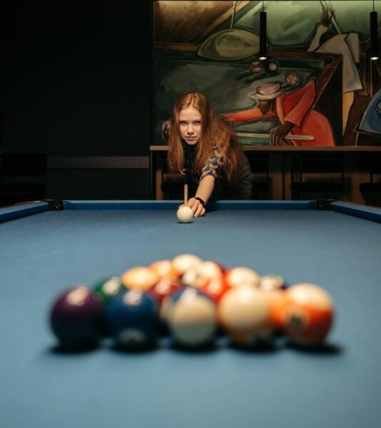 Woman focusing on a cue ball shot on a vibrant billiard table in a stylish pool hall.